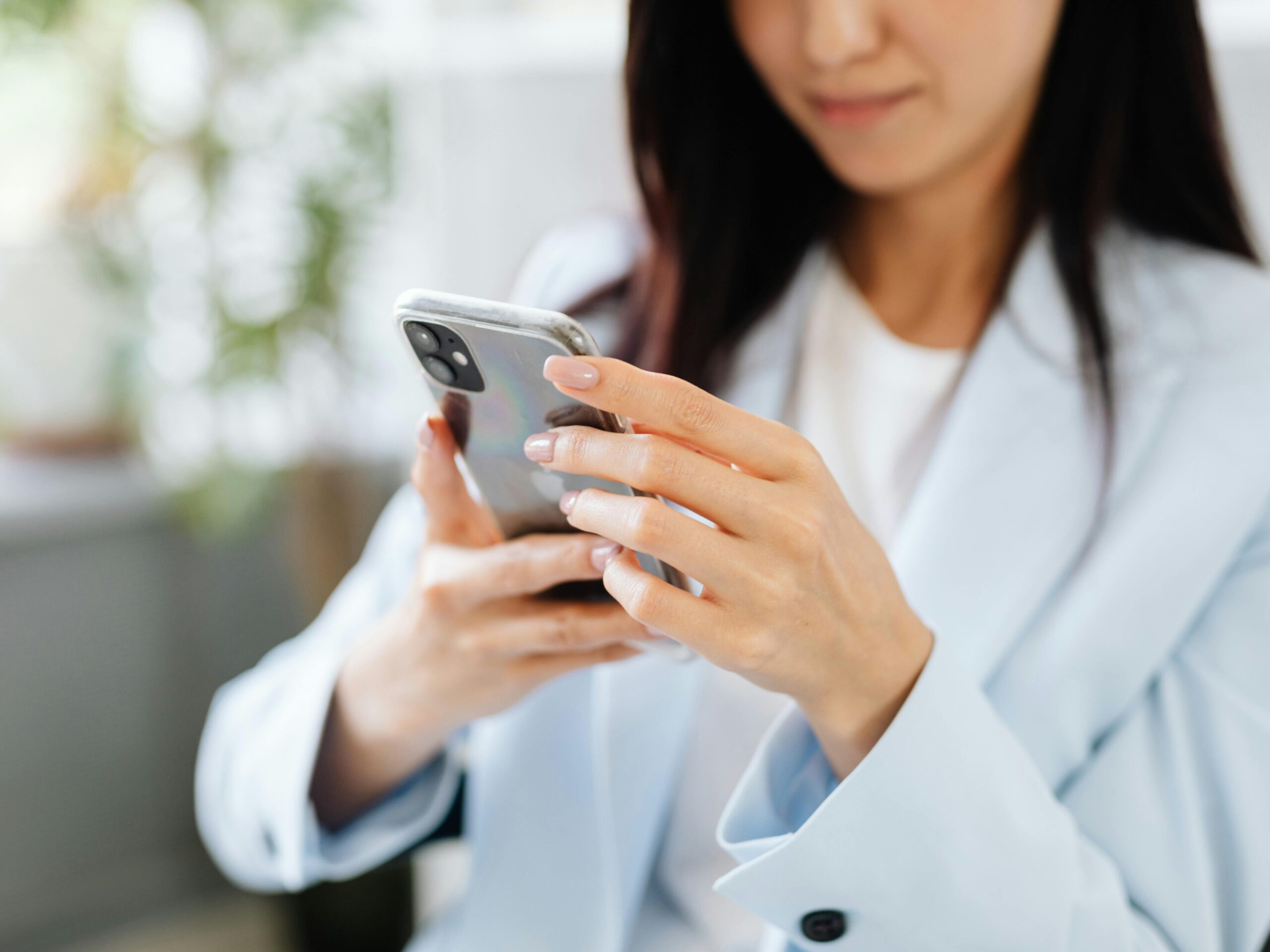 A woman with manicured nails uses a smartphone inside a modern setting.