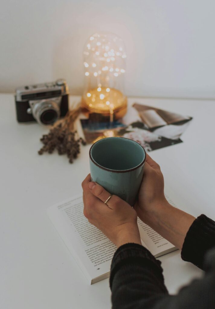A person holds a cup while reading at a cozy indoor setting with warm lighting.